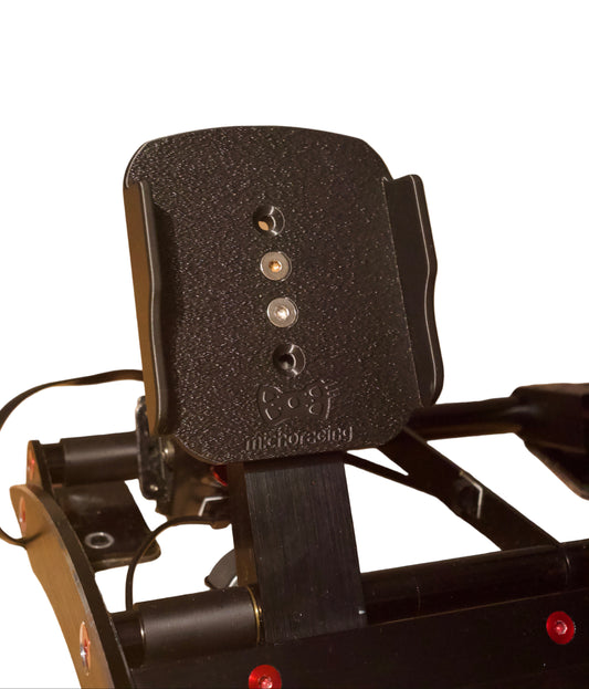 Close-up of a black simracing pedal with brand name on a wooden floor.